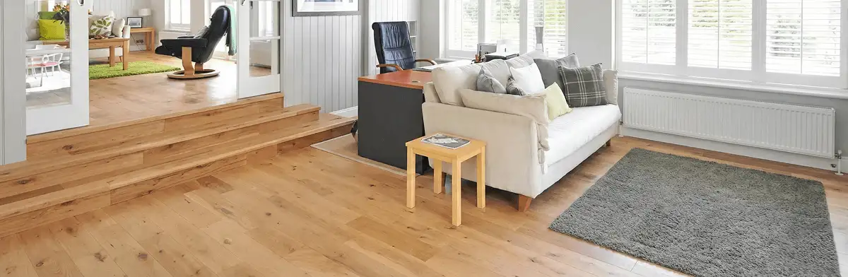 A modern living room with professionally installed laminate flooring, a beige sofa, a small side table, a gray rug, and large windows with white shutters in Rochester, NY
